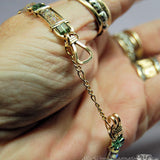 A gold-filled wire-wrapped bracelet with green gemstone accents, shown being worn on a hand with other rings also visible.